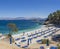View of Bataria white sand beach with blue sunbeds and tourist people at Kassiopi Bay, and Albanian mountains from the
