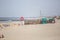 View at the beach with people taking sunbath on beach, lifeguard lifebuoys and a beach bar, lighthouse as background