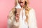 View of beautiful blonde woman in faux fur white coat with decorative ice cream showing tongue isolated on pink