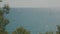 View of the beautiful blue Mediterranean sea with rocks near the shore with waves on a sunny day with boats and sailboats