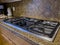 view of a beautiful gas stove top with black knobs against a square tiled backsplash