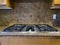 view of a beautiful gas stove top with black knobs against a square tiled backsplash