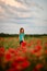 View of beautiful young woman with turned back head who standing on field with red poppies.