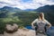 View from behind of a female hiker standing on the top of a mountain overlooking a beautiful scenic rocky mountain landscape and a