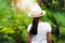 View from behind a girl wearing straw hat standing in the palm garden under sunlight