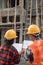 View from behind of male and female asian contractors standing wearing safety helmets holding the site plan building