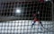 View from behind the net of the gate at a male hockey player scoring a goal. An athlete in uniform and skates plays