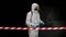 View from behind the signal tape a man in a protective uniform and a respirator with a high pressure apparatus walks and