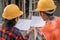 View from behind of two Asian contractors standing in safety helmets holding the site plan building