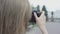 View from behind of young bespectacled female with straight blonde hair taking pictures of park alleys and monument on