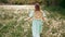 View from behind. Young stylish woman in vintage dress and straw hat walking alone on nature in countryside. Carefree