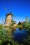 View beyond green reed grass over water canal on one isolated old windmill with reflection against deep blue cloudless summer sky