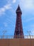 View of blackpool tower looking up from the concrete sea wall with railings in summer sunlight with blue sky