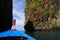 View on blue decorated wooden bow of longtail boat and passage between rock walls on both sides under blue sky