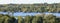 View of blue lake amongst lush green trees yellowing in autumn