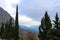 View of blue misty mountians and valley and twisting road framed by cedar and popular trees from ruins at Delphi Greece