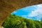 View of the blue sky and forest from under the arch of the stone bridge