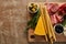 View of board with breadsticks, cheese and antipasto ingredients on brown background