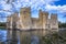 A view of Bodiam Castle ruins surrounded by water with blue sky on a sunny autumn day