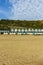 A view of the Boscombe Beach with sandy beach, colorful beach huts along the promenade with cliff under a beautiful blue sky and