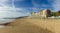 A view of the Boscombe Beach with sandy beach, colorful beach huts and building under a beautiful blue sky and some whites clouds