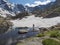 View from Bremer Hutte on man hiker standing in lake from melting snow tongues and snow-capped moutain peaks, lush green