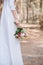View of bride in white attire holding wedding bouquet in forest