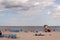 View at the calm sea with small waves, the sky full of fluffy clouds and people lying on the beach on their towels relaxing, sunba