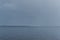 view of the calm undulating blue water of Lake Baikal, mountains on horizon, gray sky, shower, rain