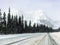 A view of a car driving down an empty highway in the winter with a huge snowy mountain in the backing along the icefields parkway