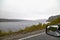 View from the car window of sad, harsh, dramatic landscape with a lake, river or fjord, a rock in the distance on the horizon and