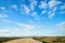 View from car windscreen with stripe relief to dirt country road, tundra and blue sky with white clouds in norht region at a sunny