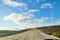 View from car windscreen with stripe relief to dirt country road, tundra and blue sky with white clouds in norht region at a sunny