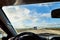 View from car windscreen with stripe relief to dirt country road, tundra and blue sky with white clouds in norht region at a sunny