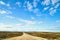 View from car windscreen with stripe relief to dirt country road, tundra and blue sky with white clouds in norht region at a sunny