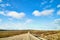 View from car windscreen with stripe relief to dirt country road, tundra and blue sky with white clouds in norht region at a sunny