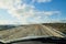 View from car windscreen with stripe relief to dirt country road, tundra and blue sky with white clouds in norht region at a sunny