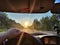 view from car windshield of natural landscape with road, green treeand and light, glare from sun at sunset in evening