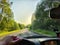 view from car windshield of natural landscape with road, green treeand and light, glare from sun at sunset in evening