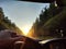 view from car windshield of natural landscape with road, green treeand and light, glare from sun at sunset in evening