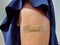 View of a caucasian girl in dark blue blouse with naked upper arm with brown bandaid after getting a dose of the COVID-19 vaccine