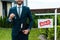 View of cheerful broker holding keys and clipboard near board with sold letters