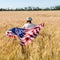 View of child in straw hat holding american flag in golden field