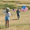 View of child in straw hat waving hand while holding american flag near father in military uniform