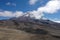 View of the chimborazo, the largest mountain on earth, with the open fields in front of it and a few clouds circeling around