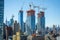 A view of a cityscape showcasing a group of high-rise buildings with construction cranes on their roofs, A city skyline during the
