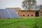 View of a clay cottage behind solar panels on a grass-covered farm