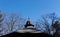 View of clear blue winter sky with decorative tiled pavilion roof and bare tree tops - with copy space in the sky