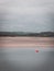 View of Clonakilty Bay at low tide. A small orange buoy is kept on a calm water surface. The sandy shore of the sea