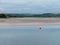 View of Clonakilty Bay at low tide. A small orange buoy is kept on a calm water surface. The sandy shore of the sea bay. The